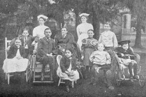A group of people containing adults in nursing uniform and children on wheelchairs