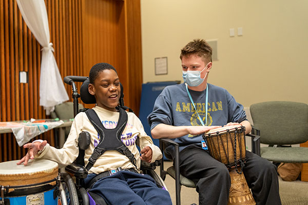 An adult and a child on wheelchair playing music with drums