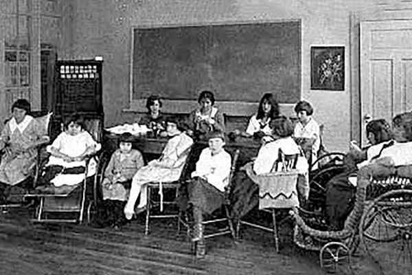 A group of children in a 1920s setting of a classroom.