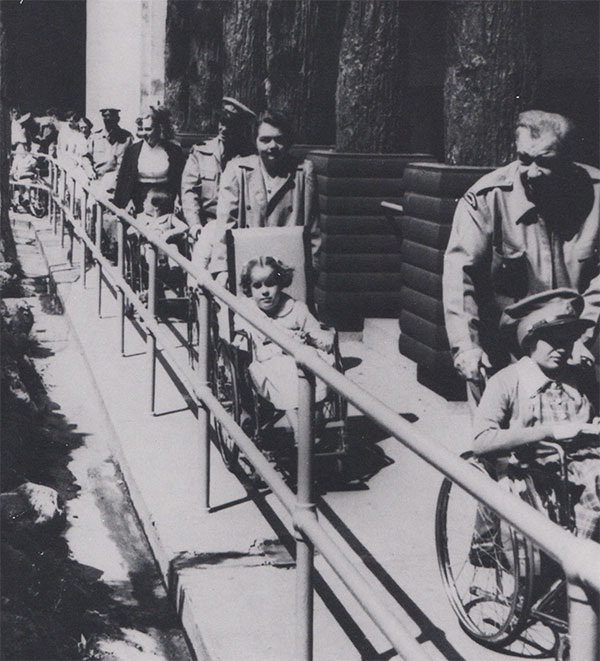 Black and white photo, some adults pushing some wheelchairs seated with kids