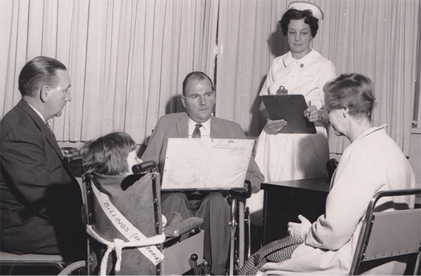 Black and white photo: some adults sitting and a nurse standing