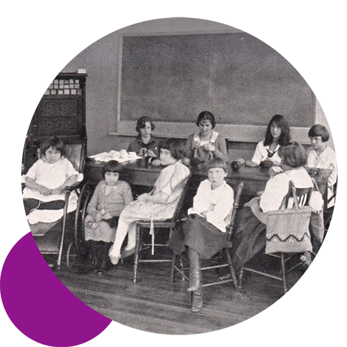 A vintage black and white photo with some adults and children in a classroom setting