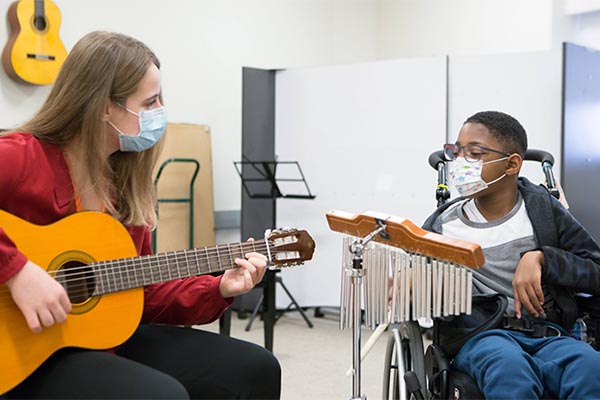 An adult and a child with mask on, playing music with instruments together.