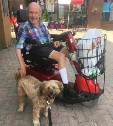 A senior sitting on a self-driven wheelchair and a dog standing beside