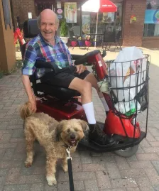 A senior sitting on a self-driven wheelchair and a dog standing beside