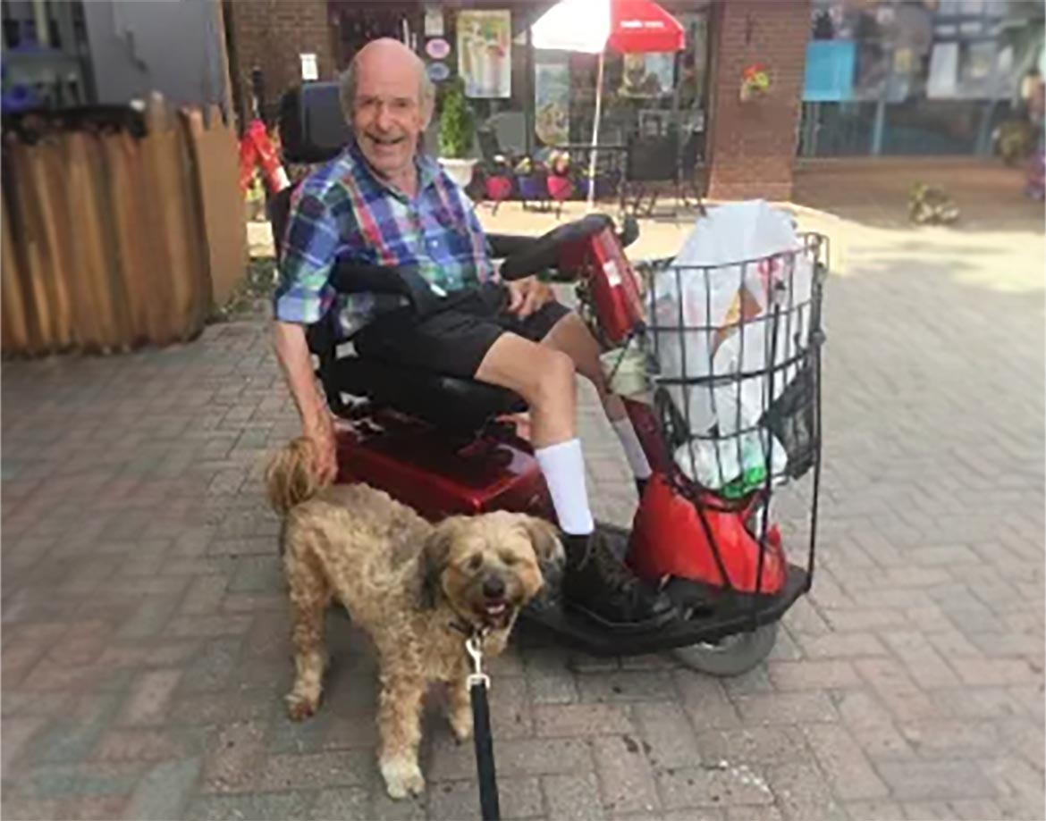 A senior sitting on a self-driven wheelchair and a dog standing beside