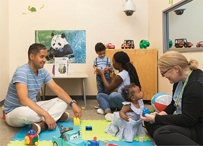 Some kids are playing in a room, accompany by some adults