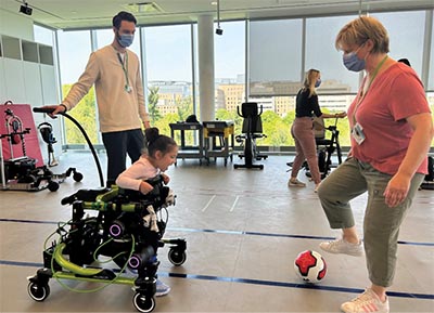 Two adults are helping a disability kid to catch a ball