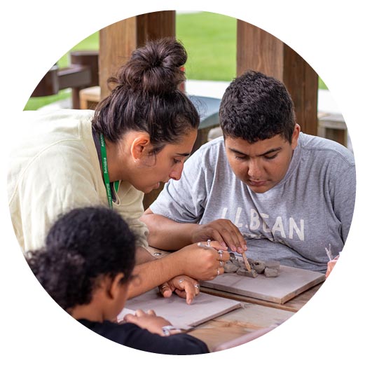 An adult is guiding two children to create an art piece